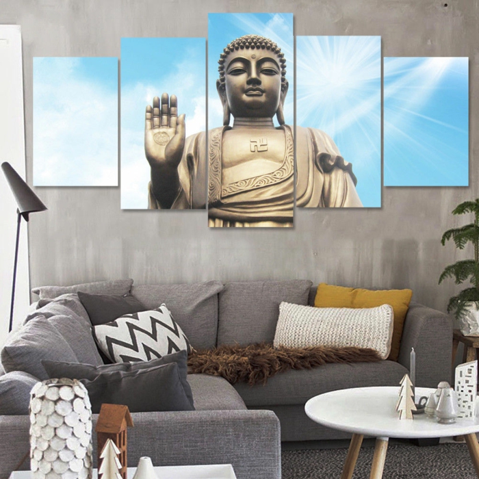 deco salon zen, ambiance zen, salon feng shui, panneau avec Bouddha qui fait sa bénédiction au mur, canapé angulaire en gris, table ronde en blanc avec des pieds en bois clair, mur en gris clair 