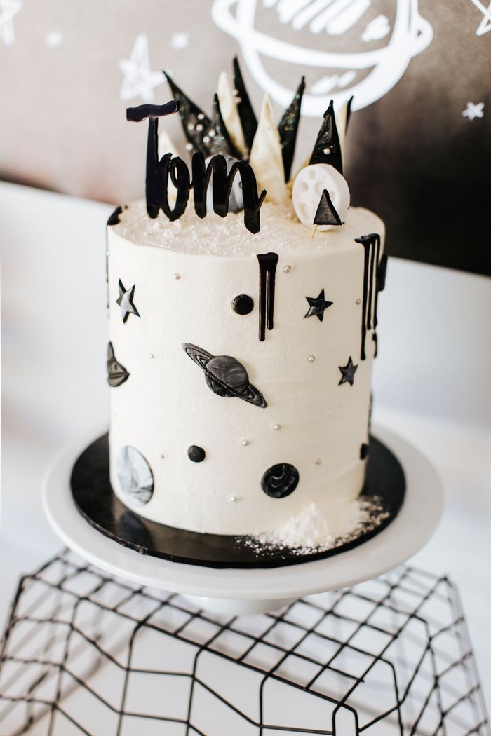 gateau d'anniversaire garçon noir et blanc sur thème galaxie recouvert de glaçage blanc et de petits détails décoratifs 