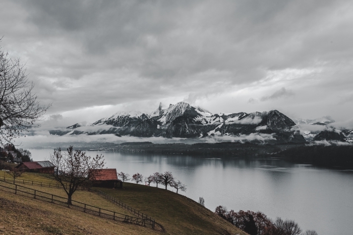 beau fond d écran avec paysage naturel, brouillard au-dessus des montagnes enneigées au bord d'un lac et champ vert