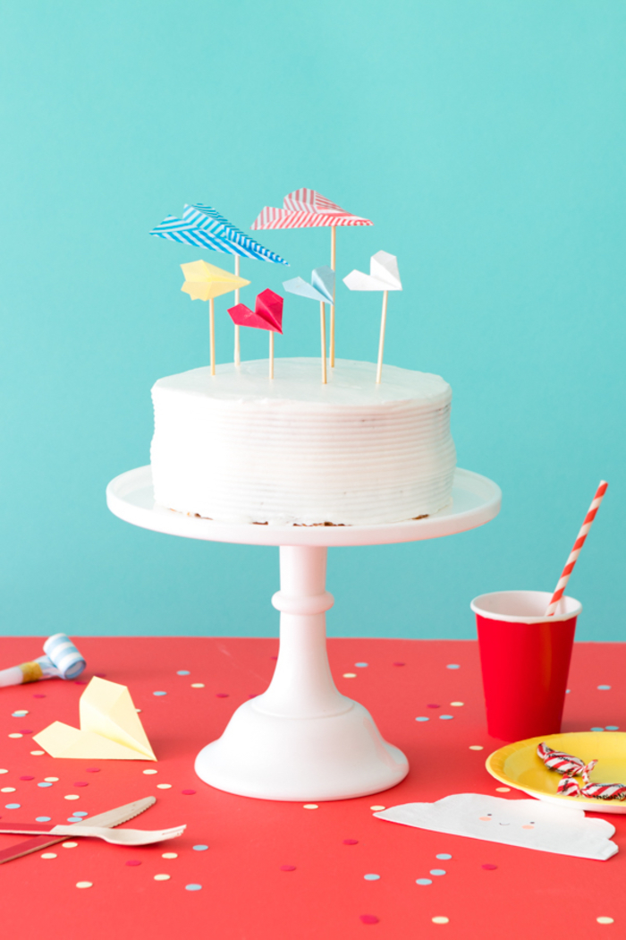 une décoration de gateau d'anniversaire au glaçage blanc avec des cake-toppers avions origami