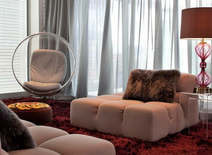 bordeau couleurn chaise oeuf suspendue, sofas bas en beige crémeux, tables acryliques gigognes et lampe rouge
