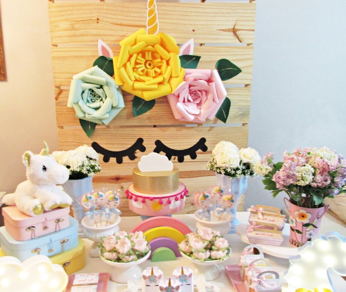 déco de buffet d'anniversaire licorne en tons pastel et fleurs sur un arrière-plan en bois personnalisé avec des fleurs en papier et des stickers yeux fermés