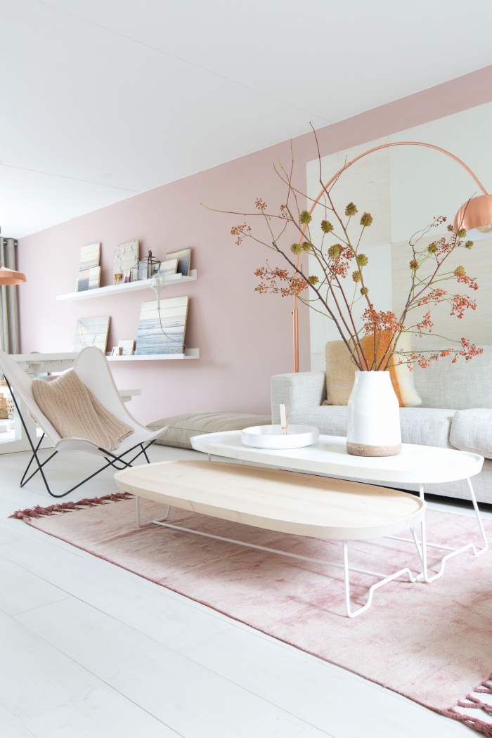 salon au plafond et parquet blanc avec peinture rose pale sur les murs, meubles blancs et bois sur un tapis rose poudré avec franges