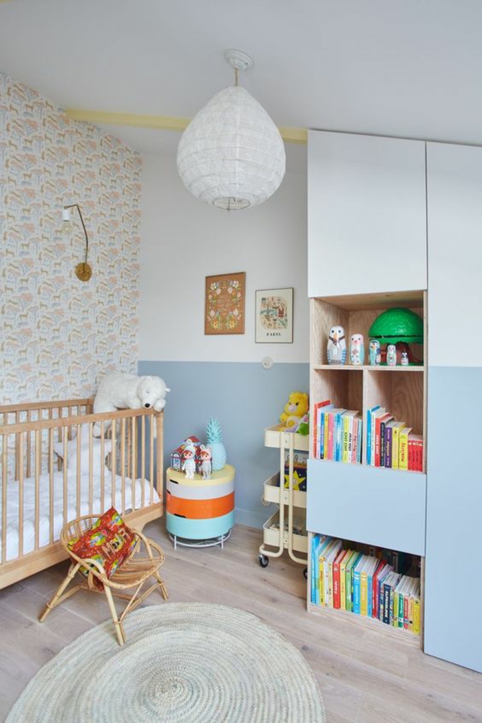 cadre chambre bébé, mur blanc, lustre chambre, tapis rond tressé, meuble moitié blanc, moitié en bleu pastel, parquet en gris, lit bébé en bois clair