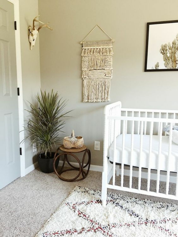 décoration chambre bébé fille, lit bois peint en blanc, murs en gris clair, petite table basse en rotin marron, tapis aux motifs losanges en blanc, rouge et bleu 