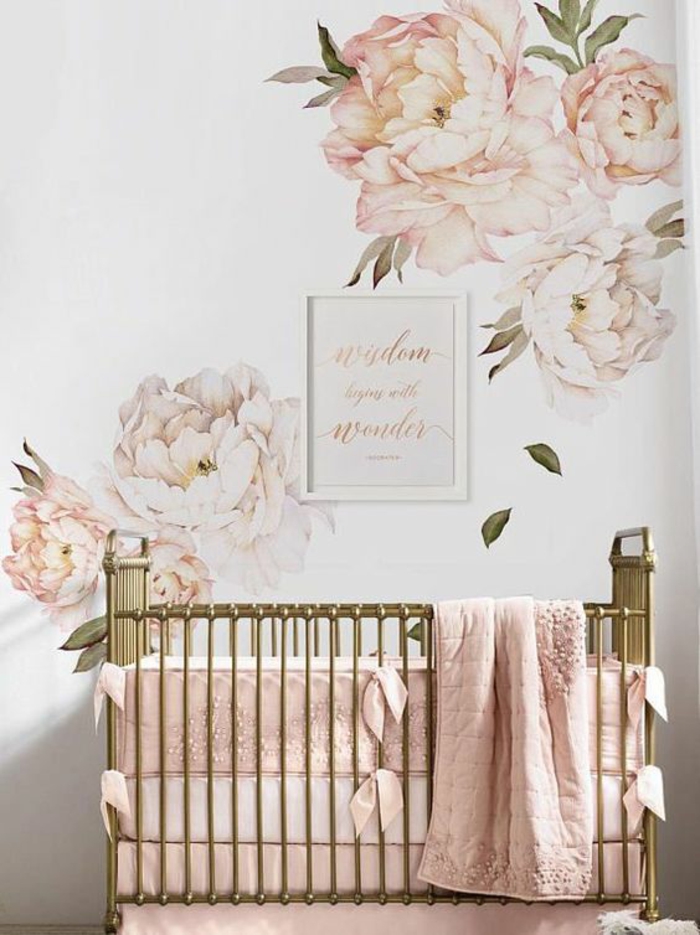 cadre chambre bébé, grandes pivoines roses sur les murs, lit en couleur bronze, cotés du lit bébé recouverts de coussins rectangulaires en tissu rose