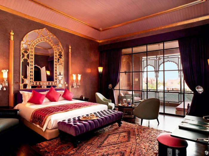grande fenêtre style atelier, miroir encadré de couleur or, trois coussins rougesn banquette lilas, tapis ethnique, plafond rose