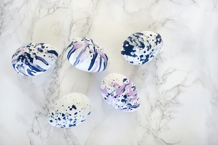 modèles de oeufs de paques à design marbre en bleu indigo violet et vert pastel sur une table à design marbre blanc et gris