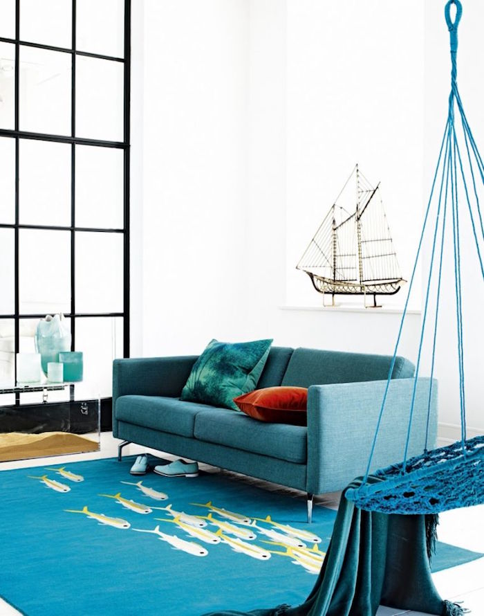 décoration de salon sur le thème de la mer, canapé couleur bleu paon sur tapis avec poissons et mur blanc
