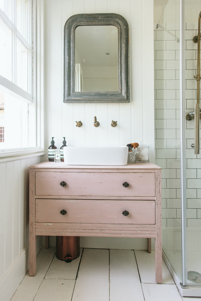 joli coin vasque d'esprit vintage chic avec une commode salle de bain rose à tiroirs, aménagée à côté de la cabine à douche