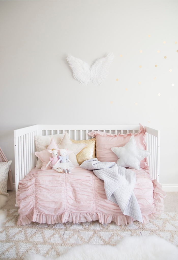 aménagement de chambre enfant fille avec lit bébé de bois blanc, couverture de lit de couleur rose poudré combinée avec coussins en formes étoiles
