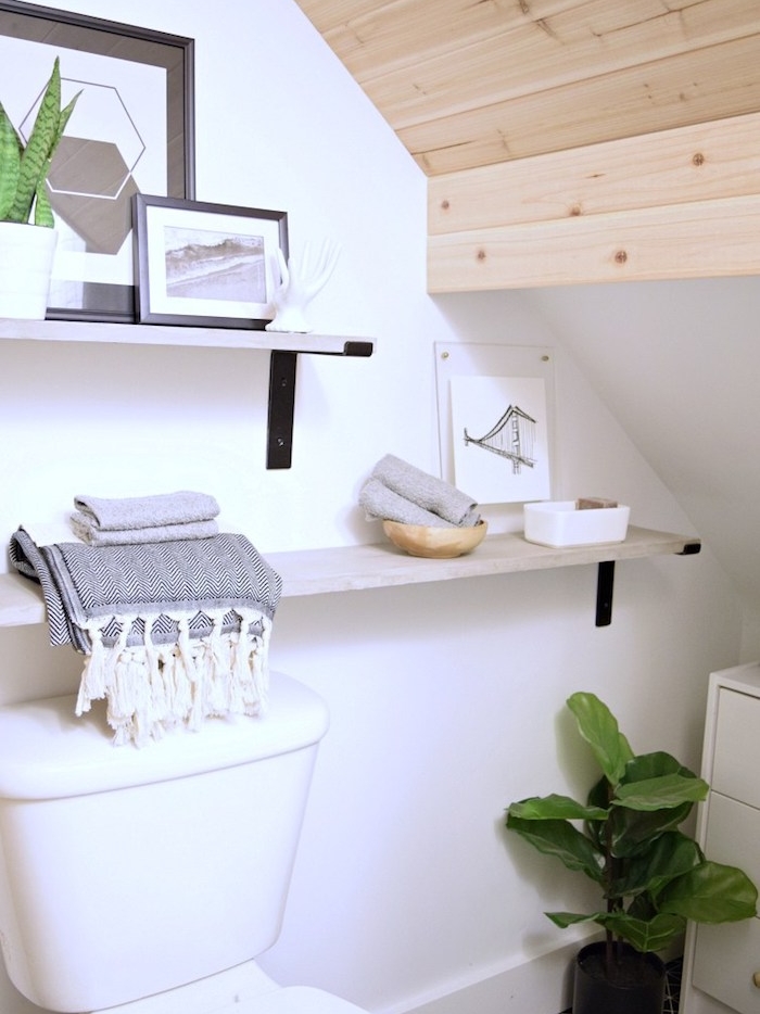 salle de bain avec des rangements au dessus du wc, plafond en bois blond, wc blanc, deco de cadres et plantes