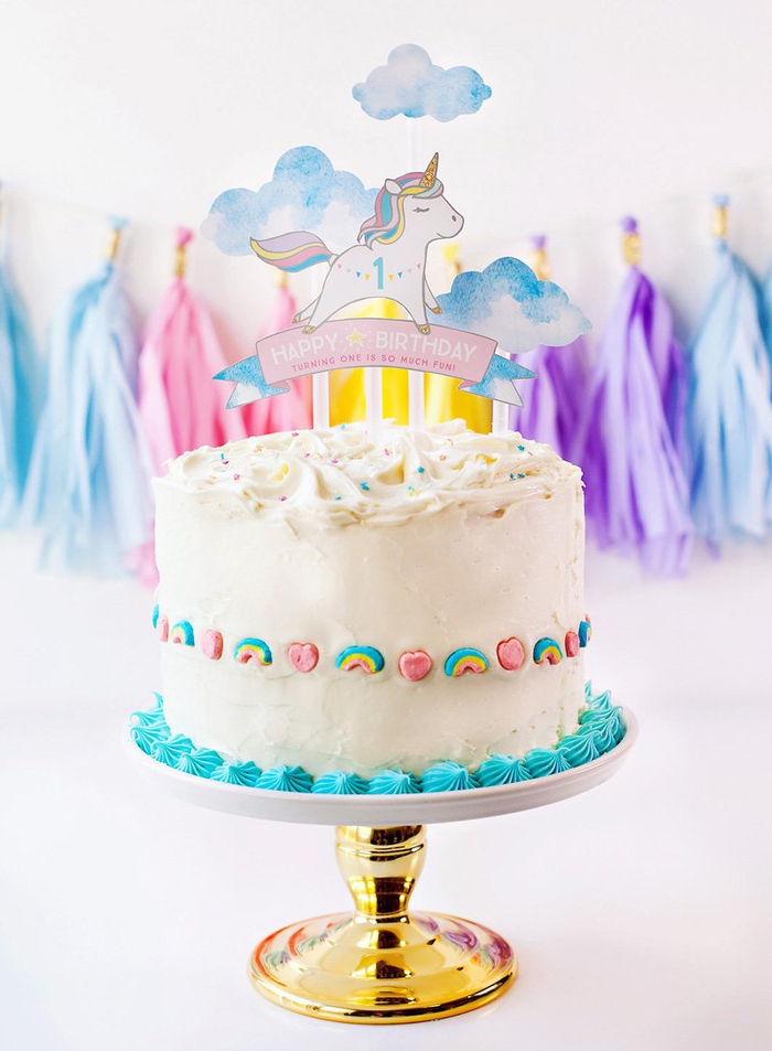gateau-anniversaire-1-an-fille-gateau-licorne-nappage-blancs-décoration-bonbons-coeur-arc-en-ciel jolie décoration de gateau licorne 1 an avec un cake-topper personnalisé et des bonbons arc-en-ciel sur les côtés