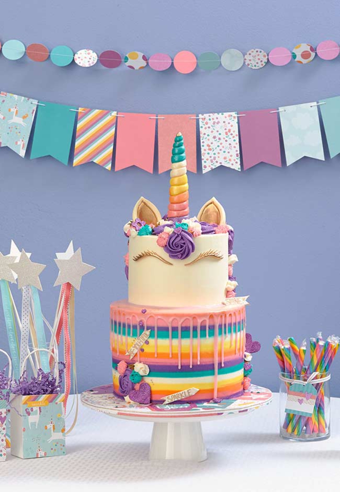 joie déco de buffet anniversaire sur thème licorne avec un gateau cake licorne à deux étages, au glaçage arc-en-ciel