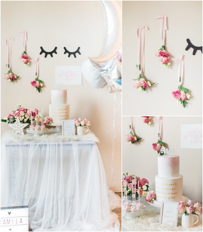 déco douce et aérienne d'un buffet d'anniversaire licorne avec une jupe de table en tulle, des bouquets de fleurs suspendus et des ballons aluminium argentés