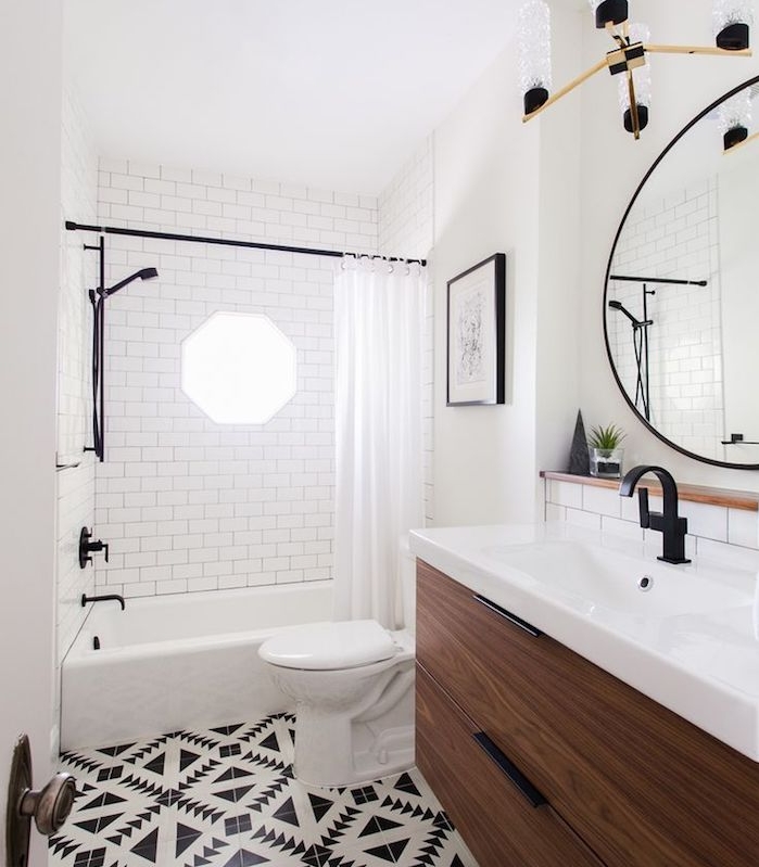 meuble petite salle de bain en bois avec lavabo blanc, grand miroir rond, baignoire avec rideau de douche, carrelage sol noir et blanc