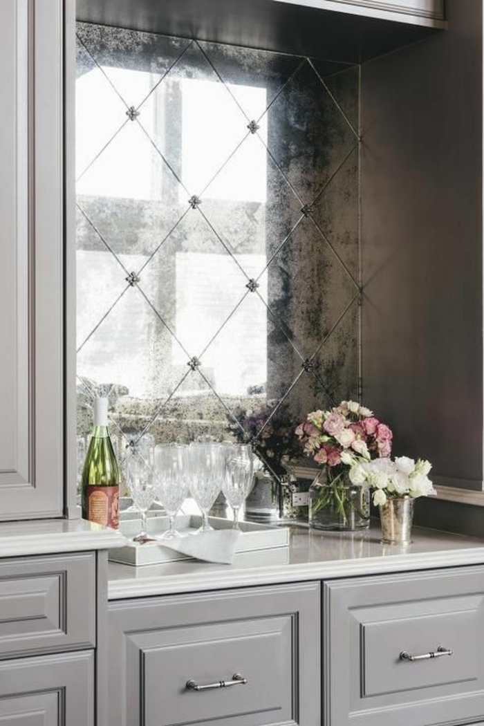 cuisine équipée moderne, amenagement cuisine, miroir vintage effet vieilli, coin décoré avec bouteille de vin, deux verres et des fleurs en blanc et rose, plan de travail blanc 