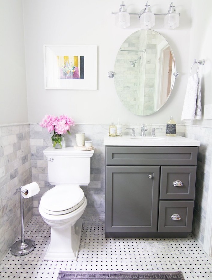 petite salle de bain design avec wc blanc, meuble sous vasque gris, carrelage sol blanc à pois noirs, miroir oval, éclairage sdb
