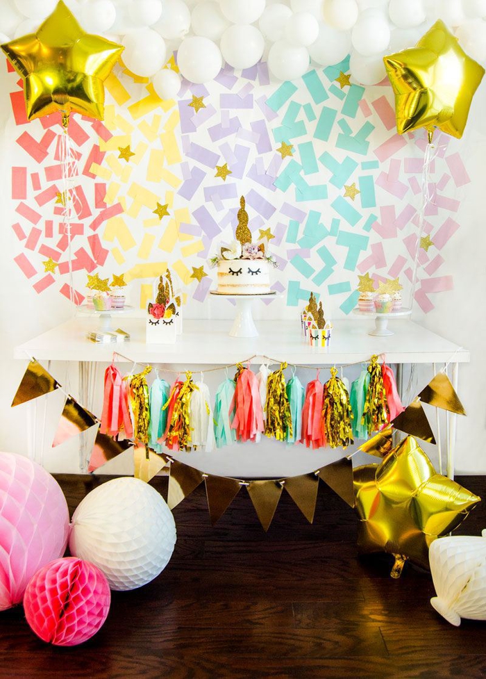 mur-en-confettis-objet-licorne-personnalisé-déco-buffet-sucré-guirlande-de-tassels-et-fanions-dorés un buffet de desserts en tons pastel et doré avec une toile de fond confettis et une jupe de table en guirlande de tassels