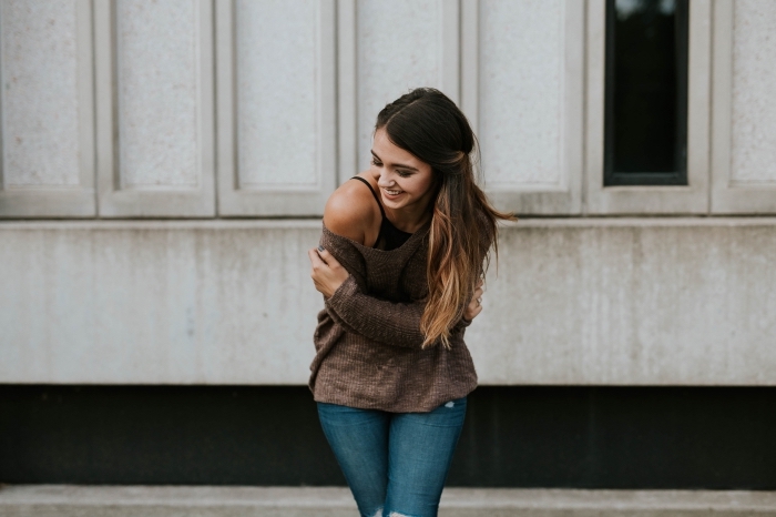 ombré hair brune, tenue comfy en jeans déchirés et pull marron avec manches tombantes, coiffure cheveux mi attachés