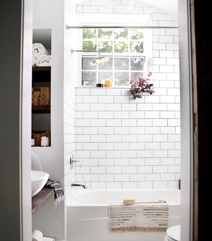 petite salle de bain avec baignoire blanche, carrelage metro blanc, niche murale avec rangements, lavabo sur une planche bois rustique
