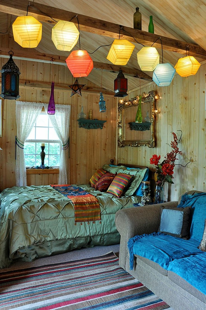 chambre gypsy à deco boheme, grand sofa bleu, lampes suspendues, plafond et murs en bois, tapis à rayures