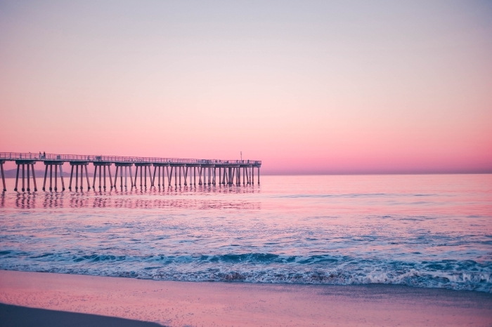 coucher de soleil au bord de la mer avec ciel rose et pont au dessus de l'eau, fond ecran paysage au bord de la mer