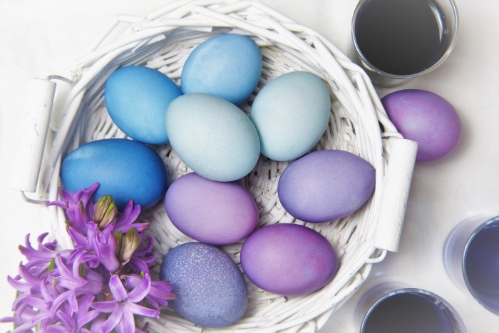 exemples d'oeuf de paque colorés en peinture alimentaire de nuances bleu et violet posés dans un panier de fibre végétal peint en blanc