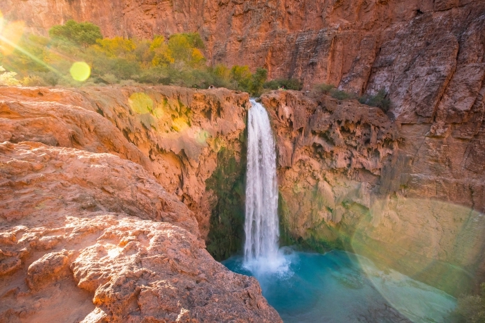 fond ecran paysage au coeur de canyon avec végétation et cascade d'eau qui tombe dans un petit lac turquoise
