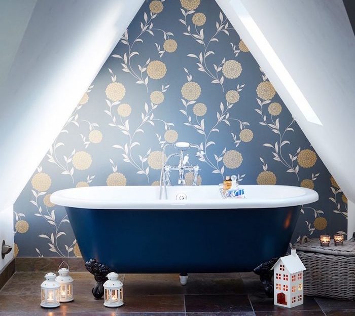 petite salle de bain design sous pente, mur décoré d un papier peint fleuri, baignoire bleu marine et carrelage sol marron foncé, deco de lanternes