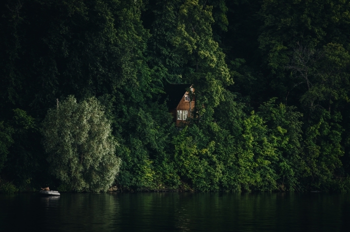 maison de bois à deux étages construite dans la forêt au-dessus d'un lac, bateau dans eau qui reflète les arbres vertes