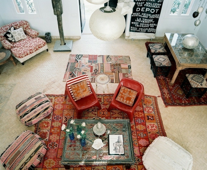 table en verre, poufs bariolés style boho chic, trois tapis ethniques, lampe suspendue blanche, table avec tabourets