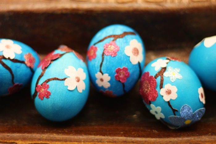 exemple oeuf a la coque avec décoration de peinture bleu clair avec fleurs et branches de papier et tissu coloré