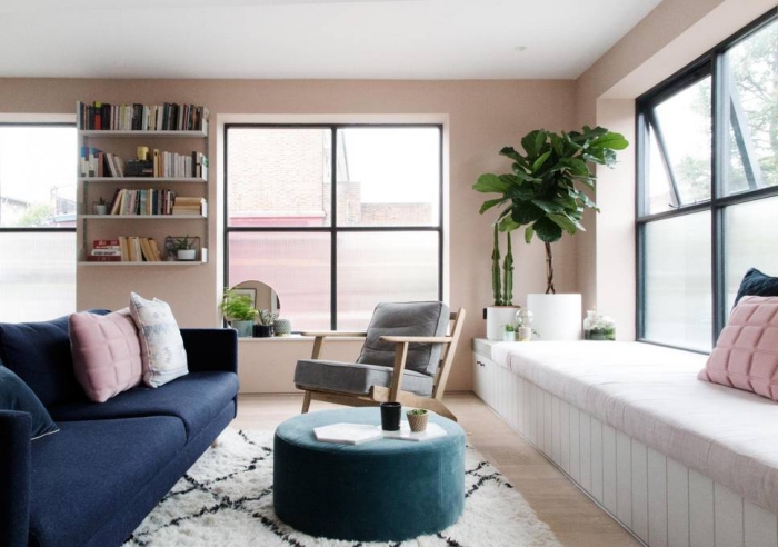salon aux murs rose poudré avec plafond blanc et parquet de bois clair, canapé de couleur bleu foncé combiné avec tabouret turquoise