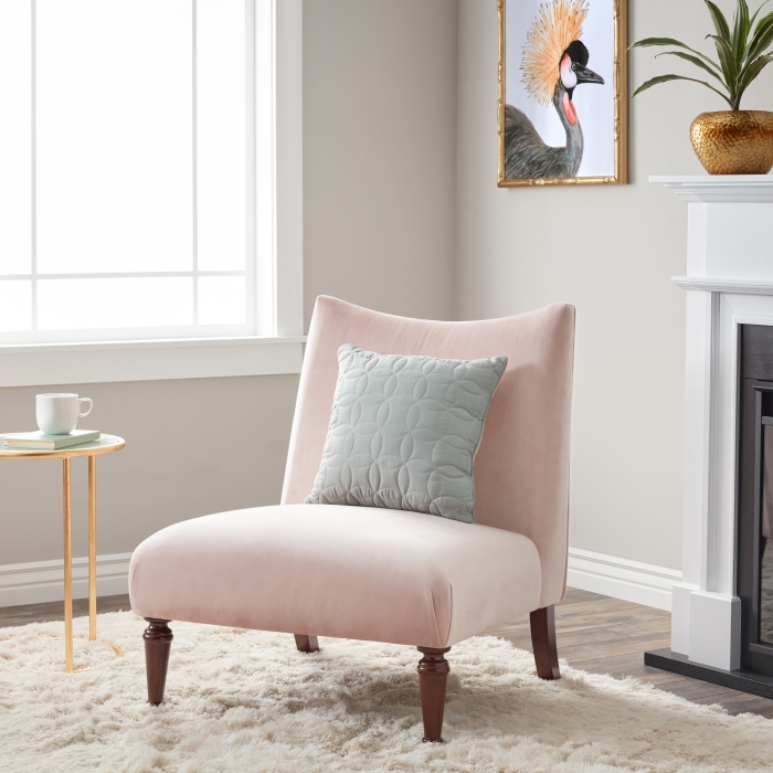 salon aux murs beige avec fauteuil de couleur rose poudré installé sur un tapis moelleux blanc, vase et cadre photo à finition cuivré