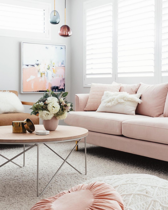 déco de salon aux murs blancs avec canapé rose poudré et table ronde basse de bois, suspension luminaire en verre