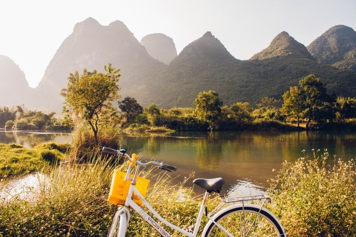 exemple de joli fond d écran avec vélo blanc et noir devant un grand lac et collines de montagnes vertes illuminés par les rayons du soleil