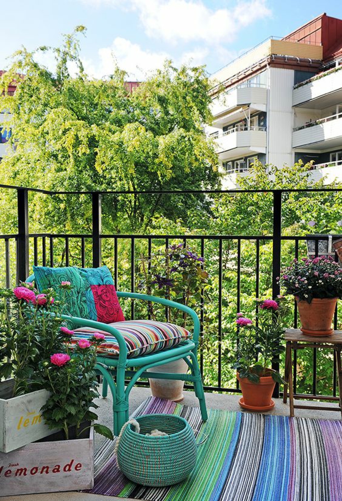 magnifique vue d'une terrasse, idée déco terrasse, idee amenagement terrasse, fauteuil en canne en vert lac, panier tressé en vert lac, tapis ethnique en vert, jaune, bleu indigo, palettes avec des fleurs