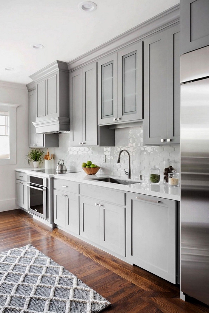 une cuisine grise et blanche aménagée en longueur où la crédence brillante et l'inox s'accordent parfaitement avec la couleur des meubles