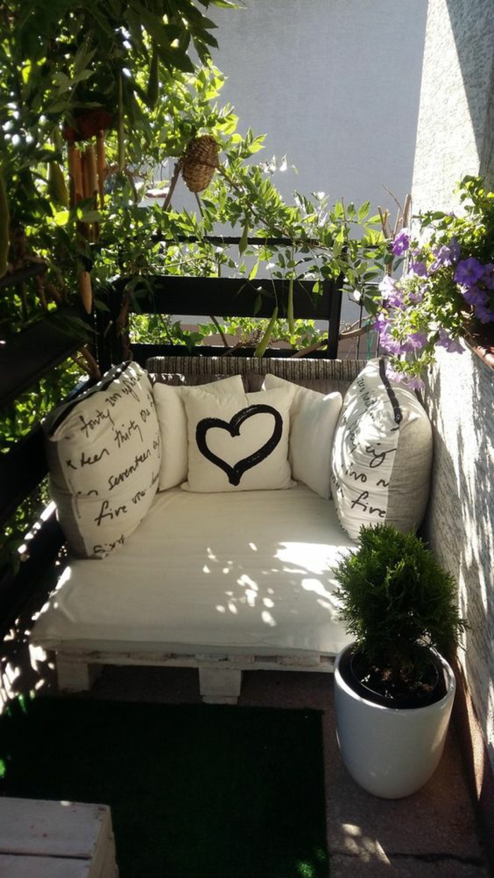 idee deco terrasse, meuble canapé en palettes peint en blanc, avec des matelas et coussins en couleur ivoire, pot blanc avec petit buisson vert, garde-corps en métal noir