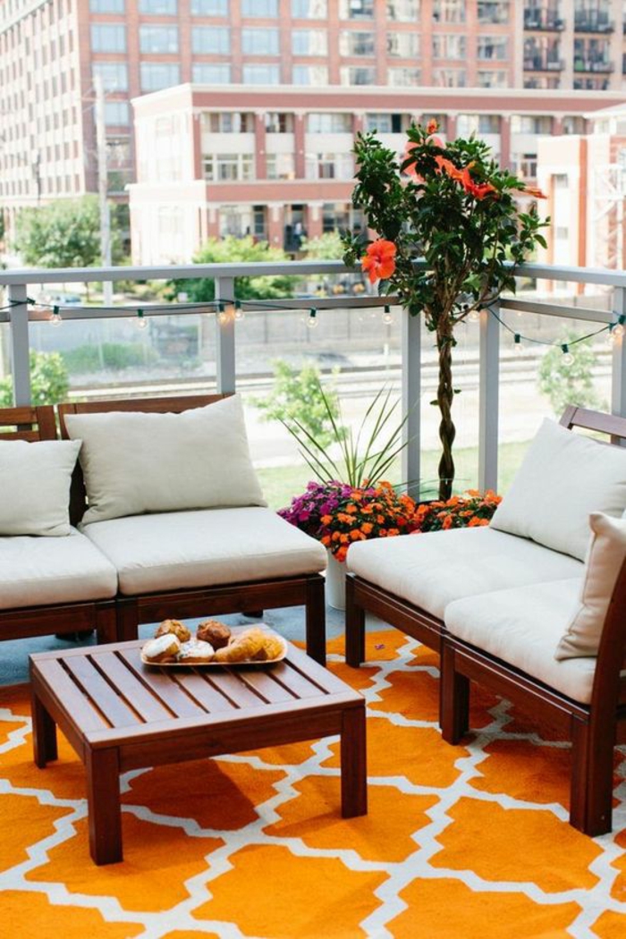 une idée déco terrasse, des meubles massifs en bois foncé en style asiatique avec table basse carrée, un arbre oranger fleuri, tapis en orange et blanc 