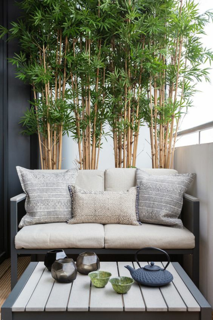 séparateur d'espace bambou, canapé en métal gris pastel rempli de coussins petits et grands, table basse avec plan en bois PVC blanc, accessoires pour le thé en style asiatique, idee deco terrasse