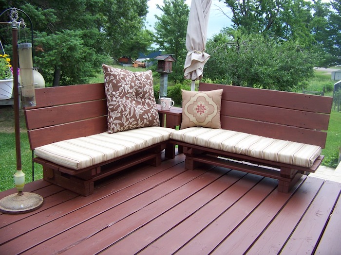 banquette palette de bois repeinte en marron avec des coussins d assise beige et marron sur une terrasse exterieure en bois