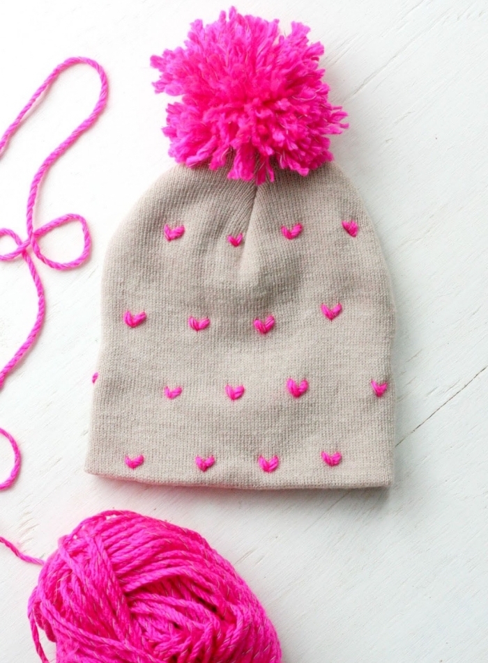 activité manuelle maternelle pour customiser un bonnet beige avec déco en fil rose en formes de coeur et pompons rose fuschia