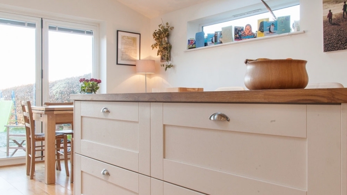 meuble cuisine avec plan de travail de bois foncé et armoires blanches aux poignées métalliques sur plancher de bois clair