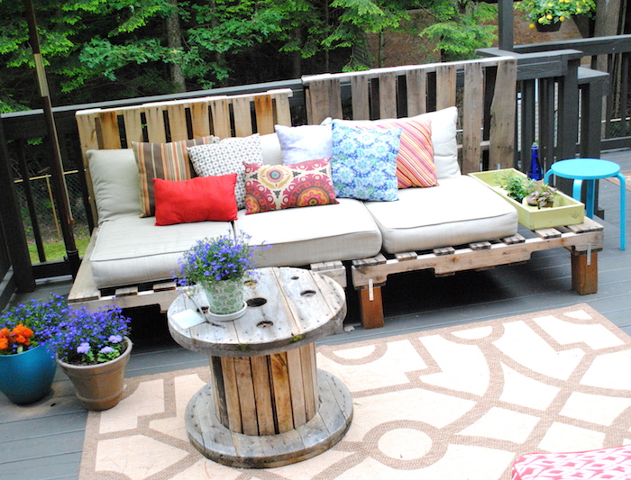 exemple de salon de jardin palette avec un canapé palette de bois avec coussin d assise gris et coussins décoratifs colorés, table touret, deco terrasse pots de fleurs