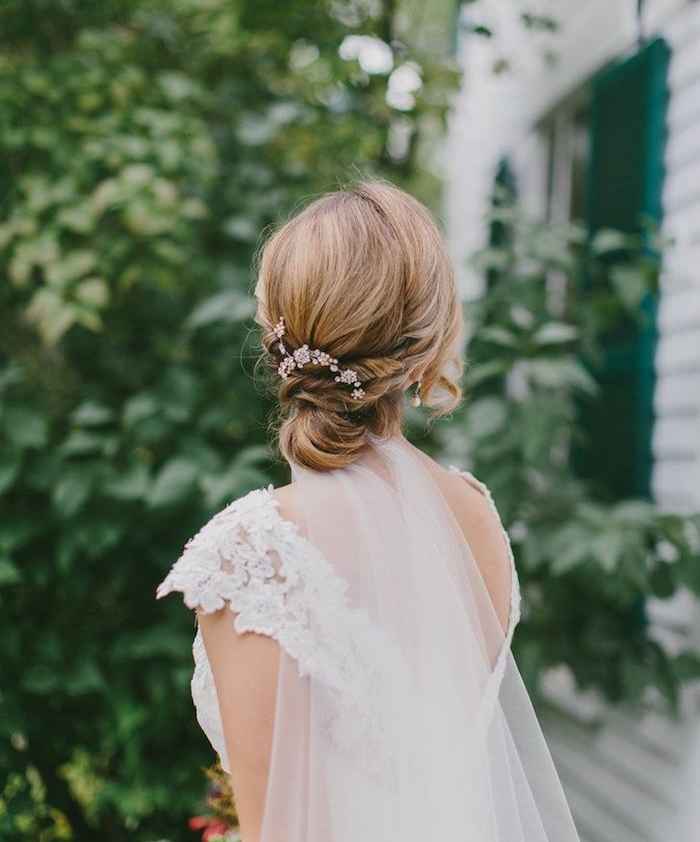 modele de coiffure femme chignon bas sur carré long avec decoration de fleurs artificielles, robe de mariée dentelle