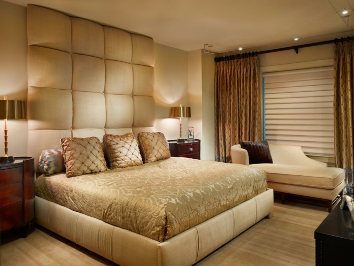 jolie chambre à coucher en couleurs neutres, rideaux lourds ocre, sofa beige, chevet en bois rouge