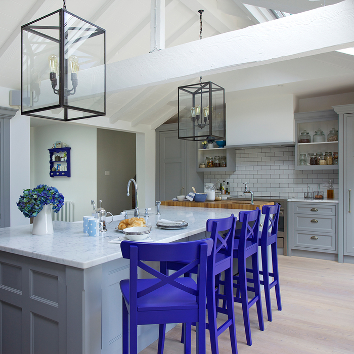 une cuisine grise et blanche de style rustique contemporaine équipée d'un îlot central par accentué par des chaises bleu de cobalt et des suspensions lanternes en verre et laiton