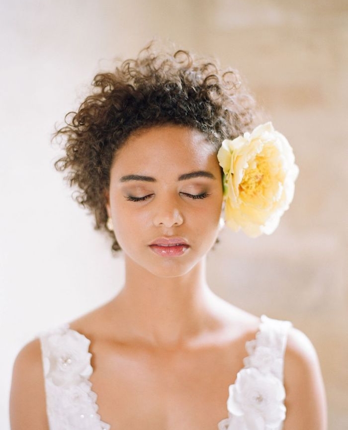 coiffure afro femme aux cheveux crépus accessoirisés d une large rose jaune de coté de la tete, robe de mariée blanche fleurie